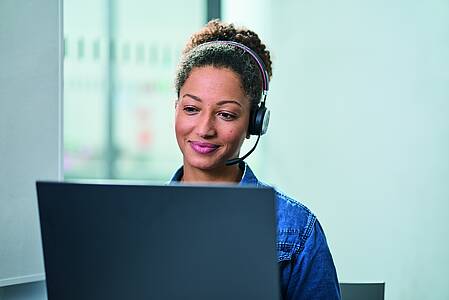 Foto einer Frau mit Headset, die am Laptop sitzt